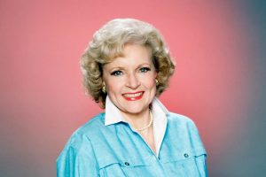 Portrait of a smiling Betty White, who is wearing a blue blouse against a pink background.