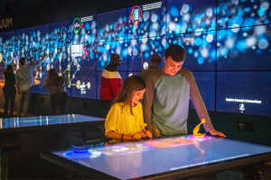 Pre-teen girl and boy at the Prop Stars exhibit, smiling and laughing at the museum content on the screen.
